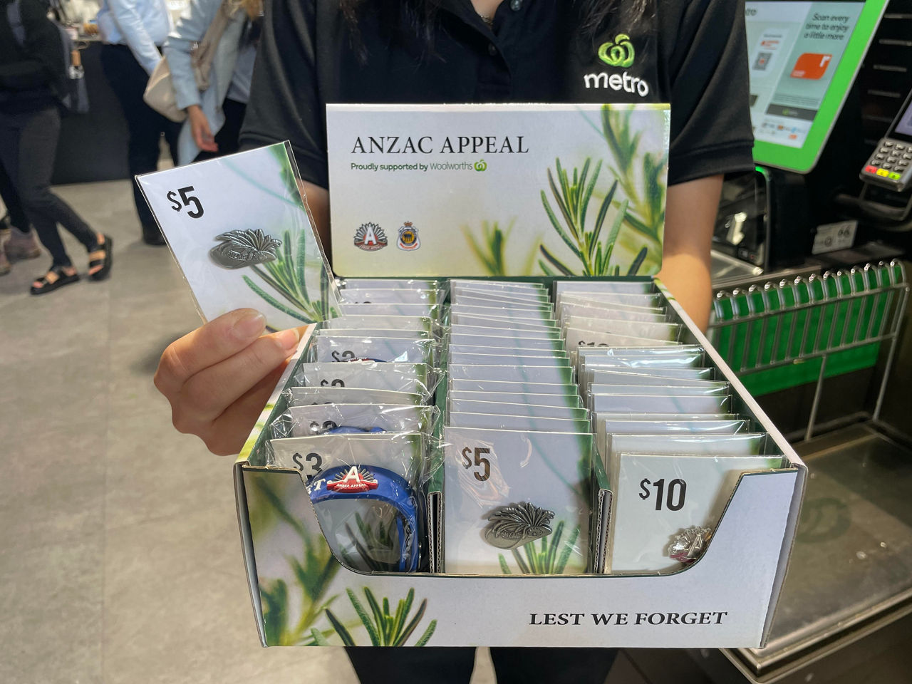 Woolworths team member holding box of ANZAC Appeak badges