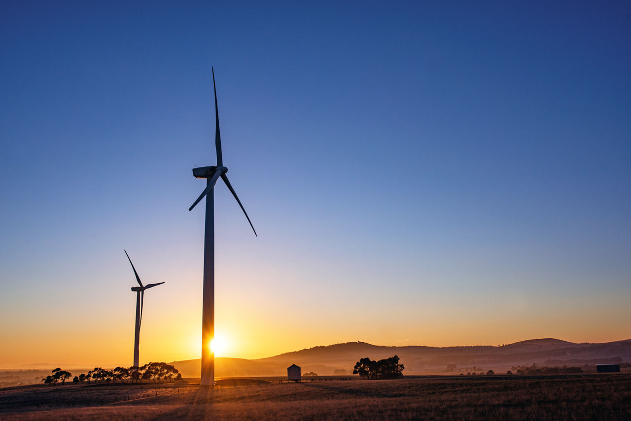 Wind turbine silhouettes with the sun shining through the turbine at sunrise.