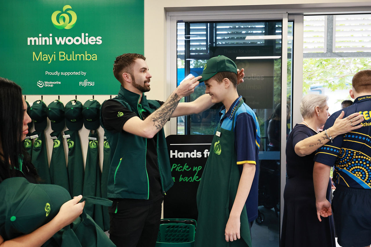 Woolworths team member helps student into a cap and apron 
