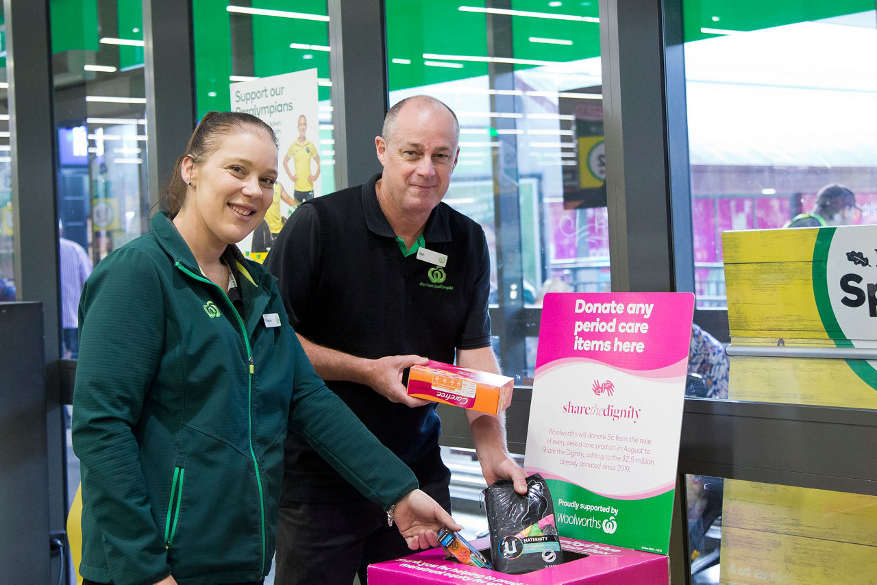 Two Woolworths team members placing period care products into donation box